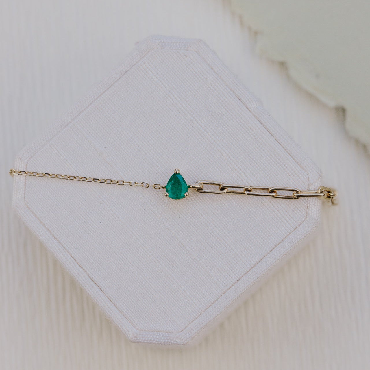Gold bracelet with a green emerald gemstone on a white hexagonal card