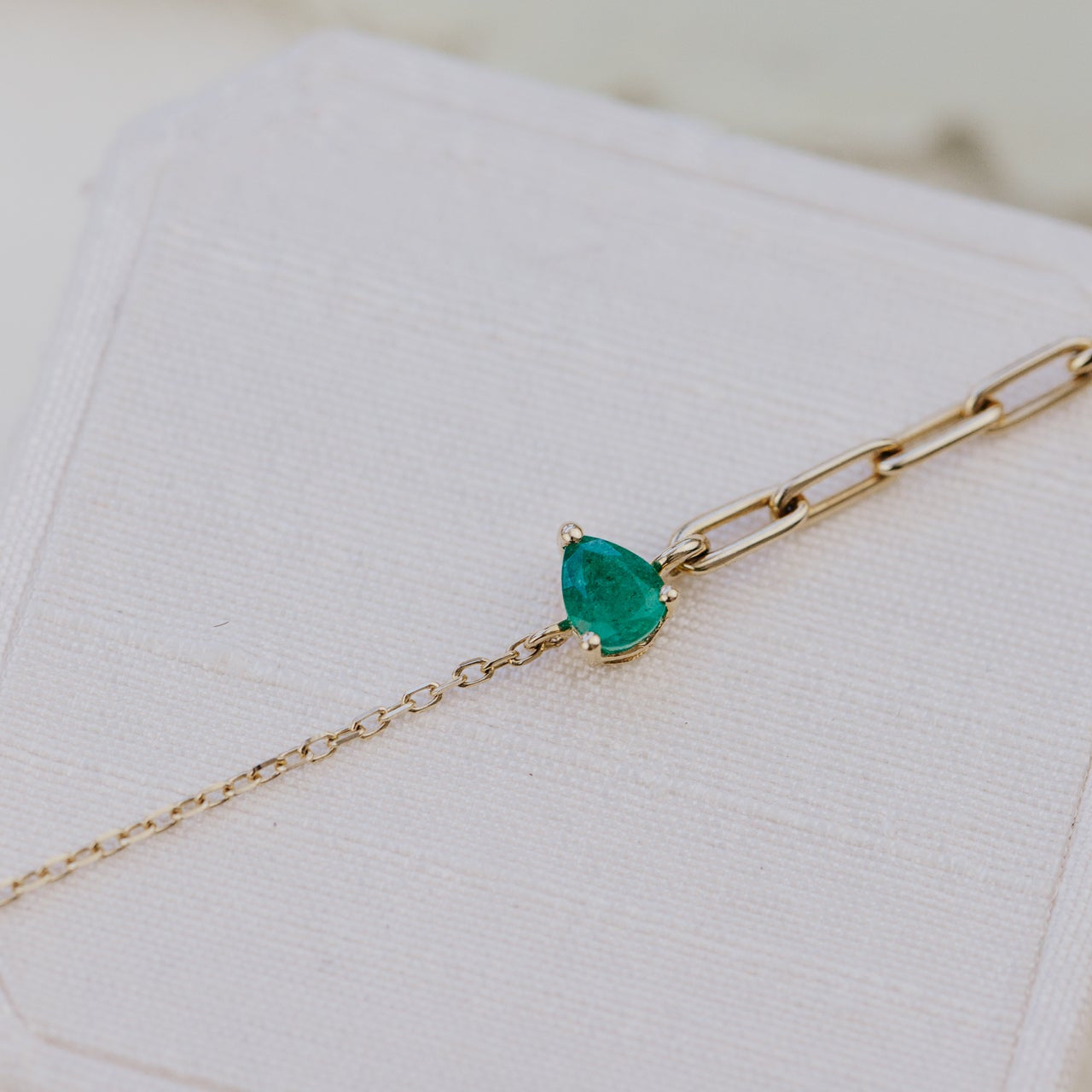 Gold bracelet with a green emerald gemstone on a white surface