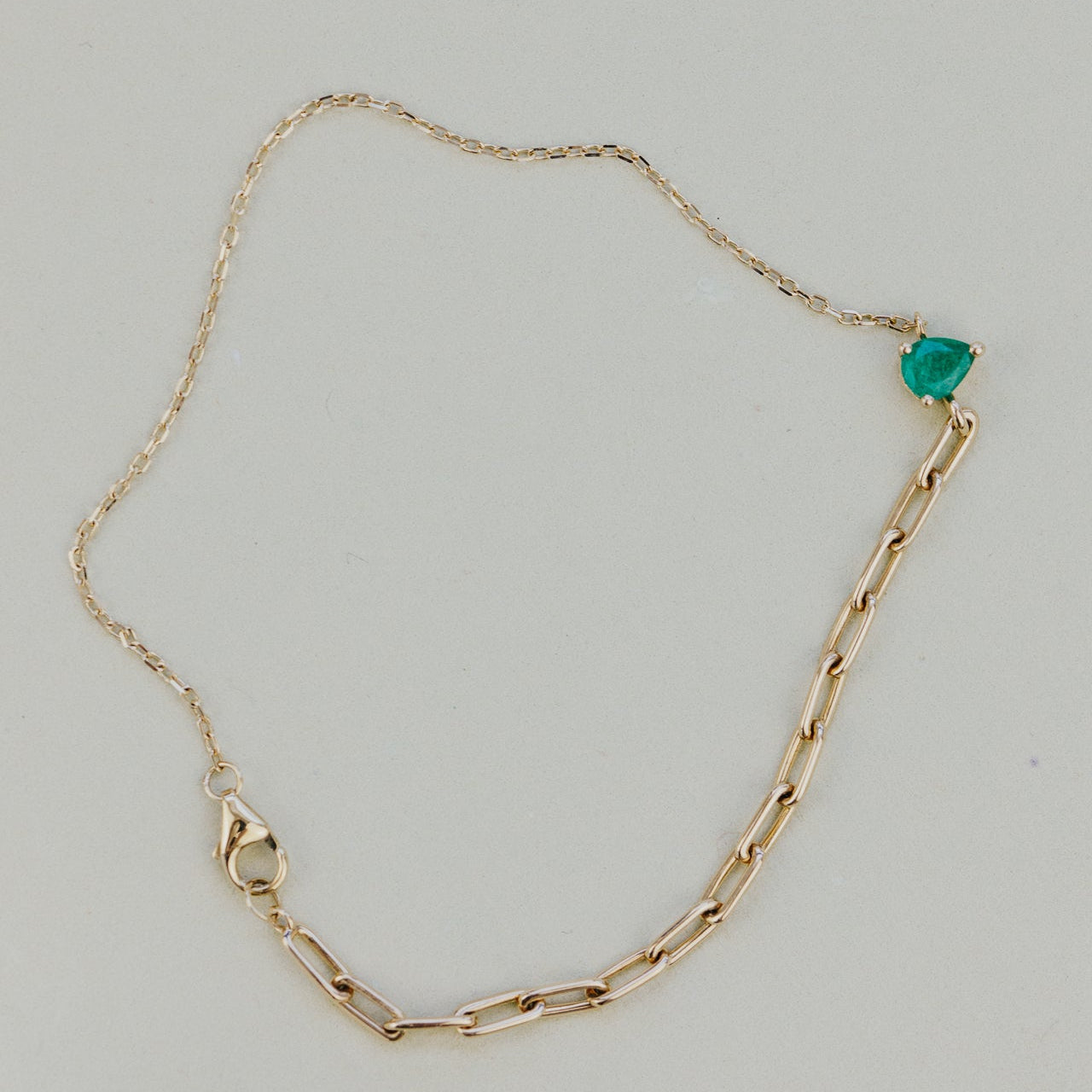Gold chain bracelet with a green emerald gemstone on a light gray background