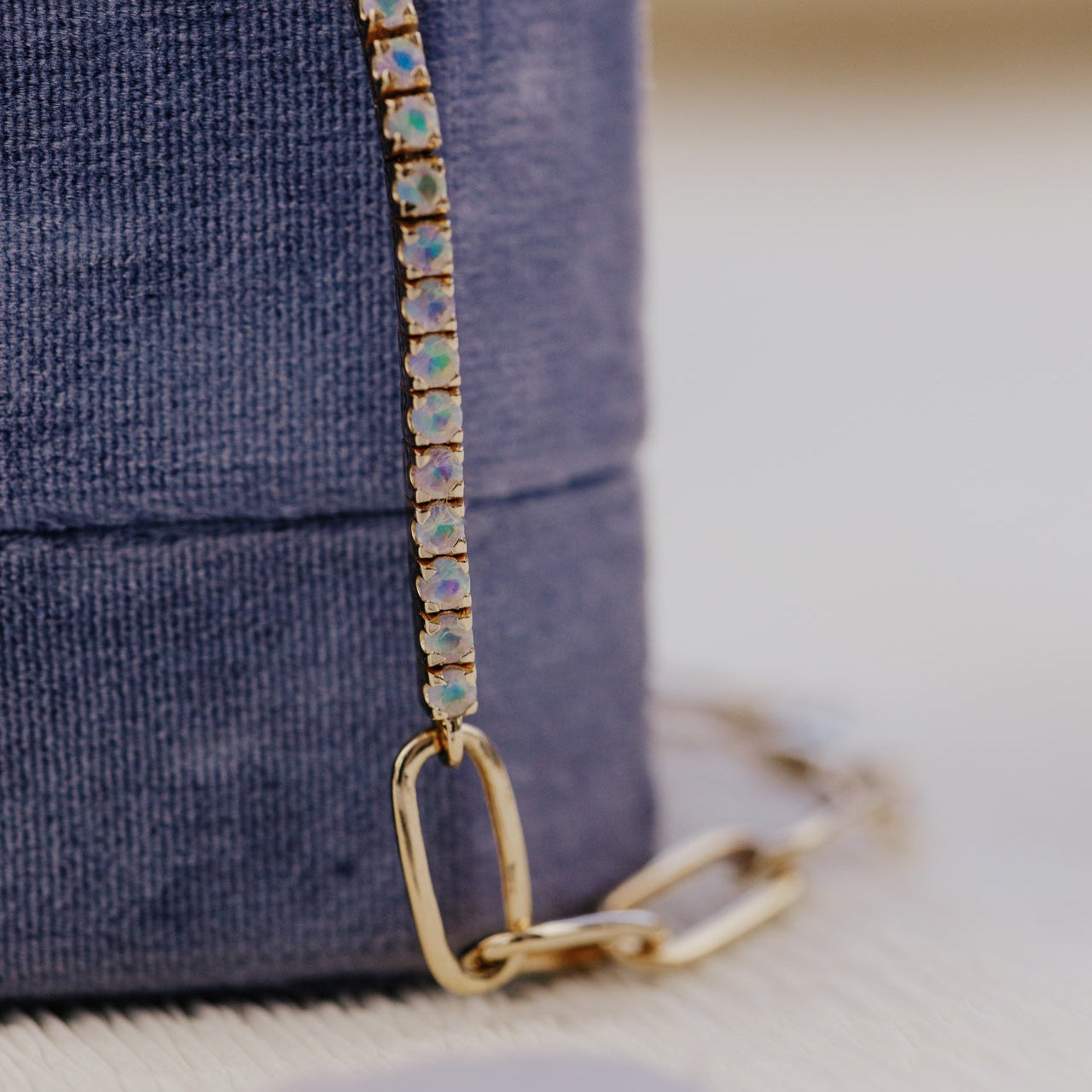 Gold chain with opals attached to a purple bag on a blurred background