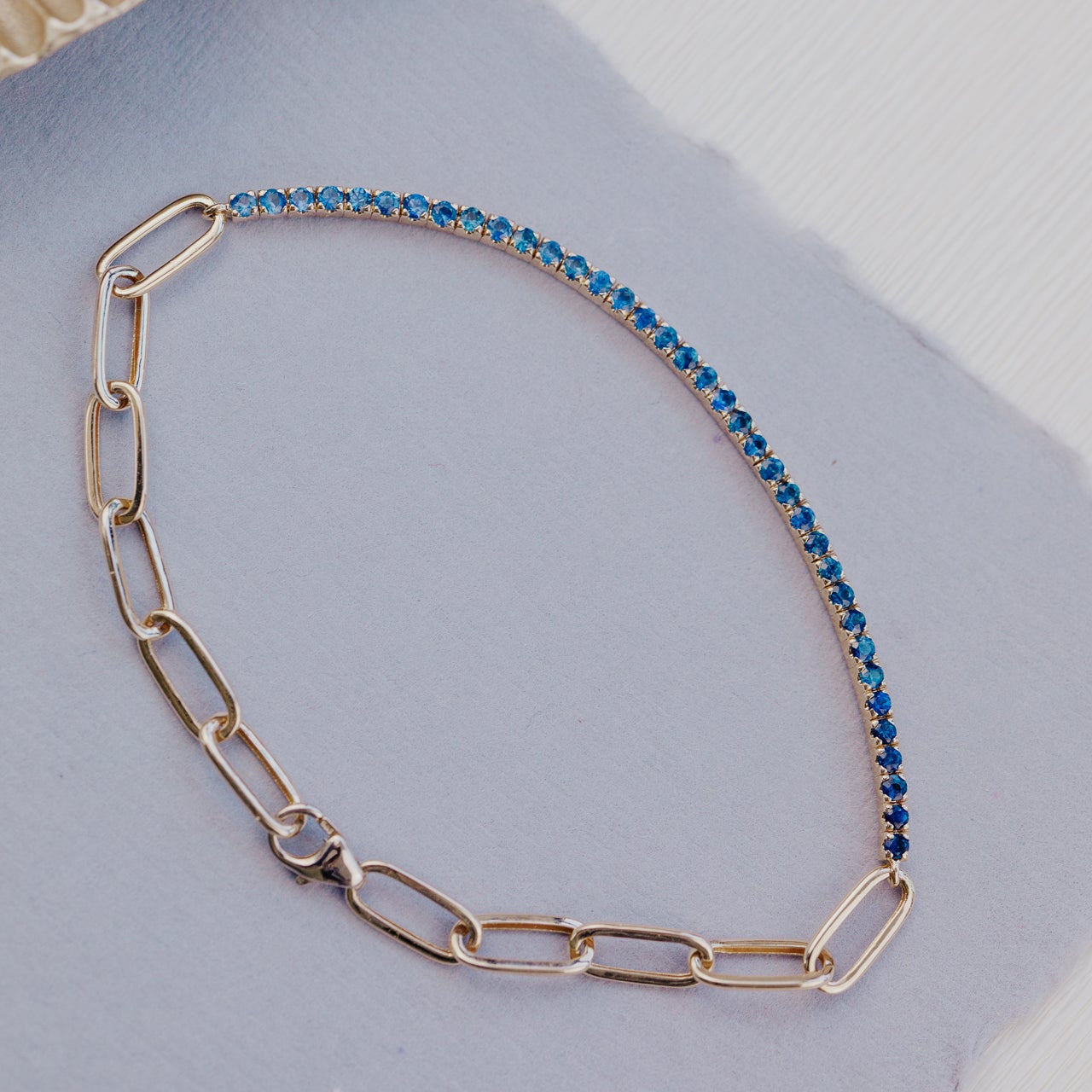 Gold paperclip chain necklace with blue sapphires on a light gray surface