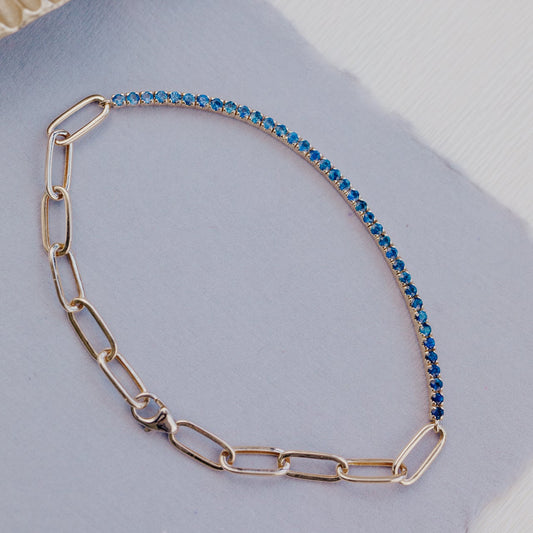 Gold paperclip chain necklace with blue sapphires on a light gray surface