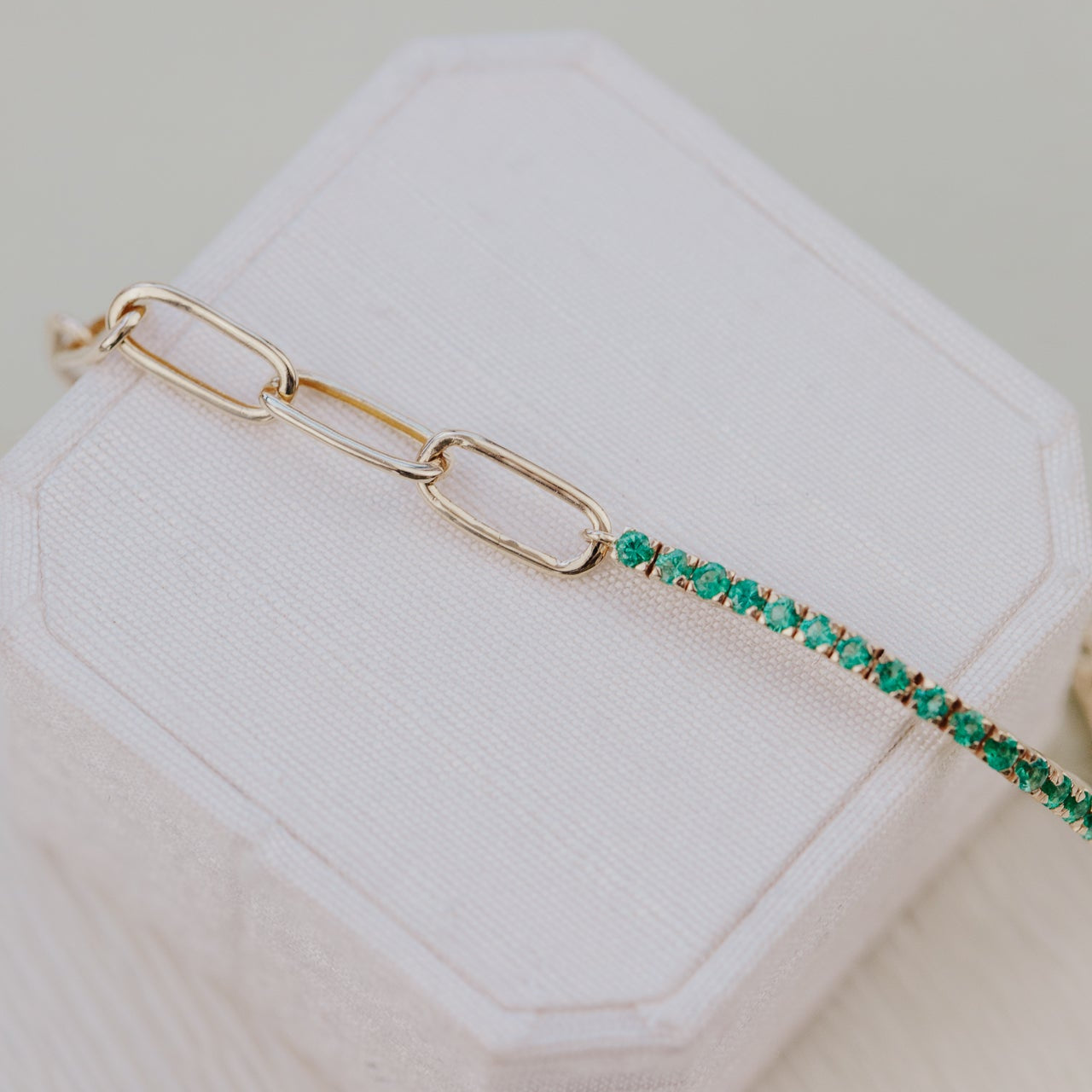 Gold bracelet with green emeralds on a white hexagonal stand