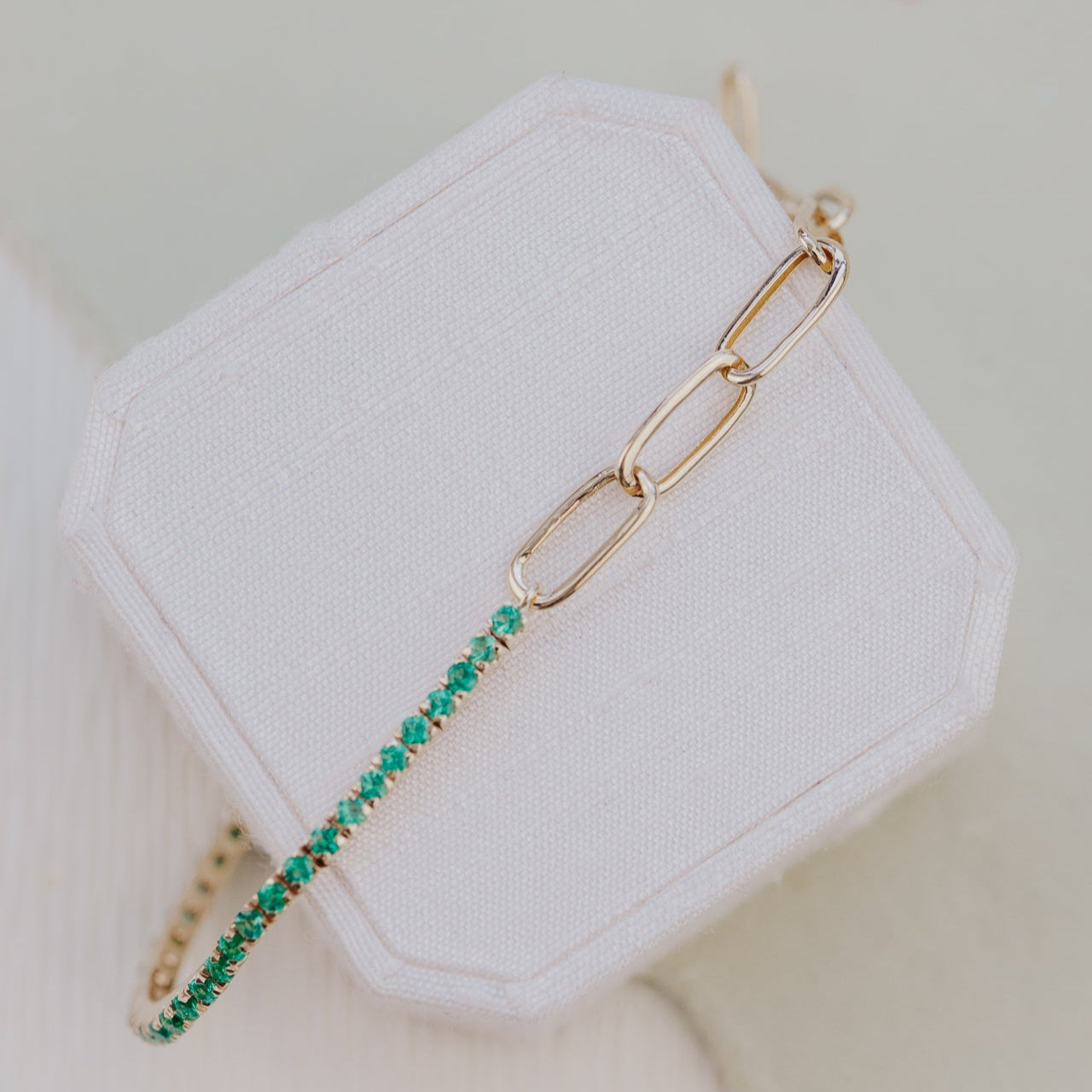 Gold bracelet with green emeralds on a white jewelry box