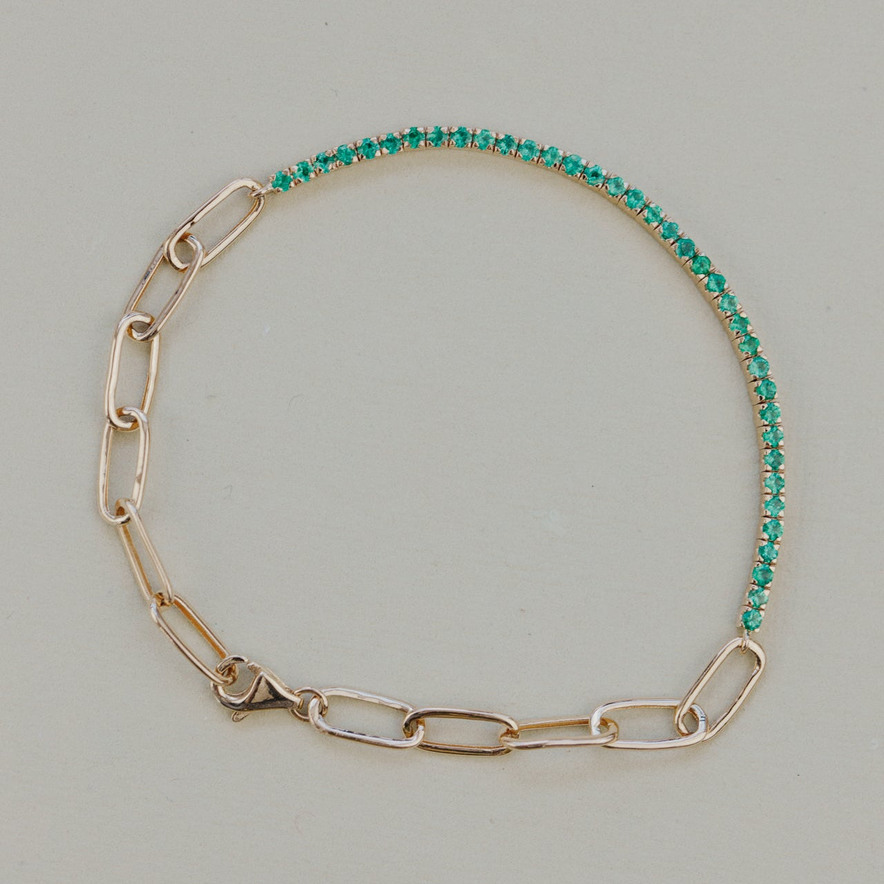Gold chain bracelet with green emerald gemstones on a light gray background