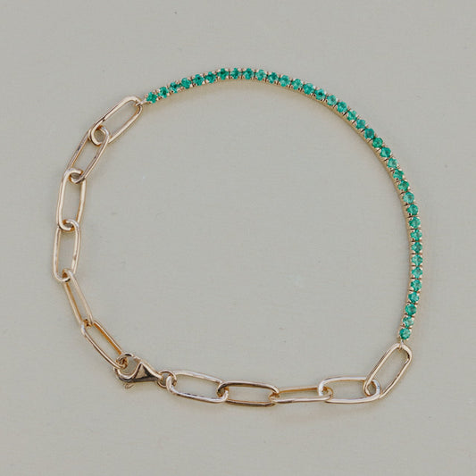 Gold chain bracelet with green emerald gemstones on a light gray background