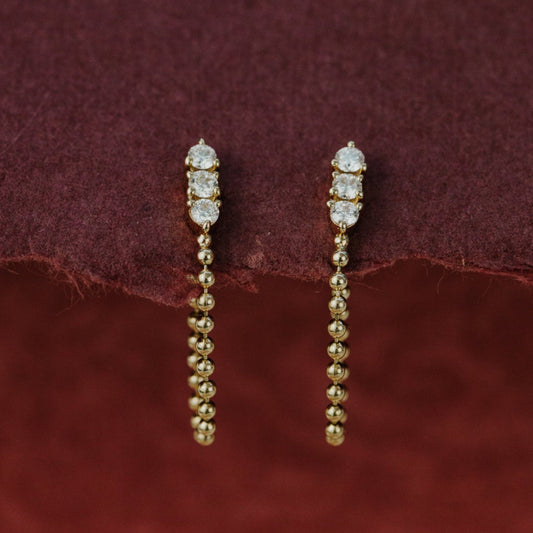 Gold earrings with beads on a maroon fabric background