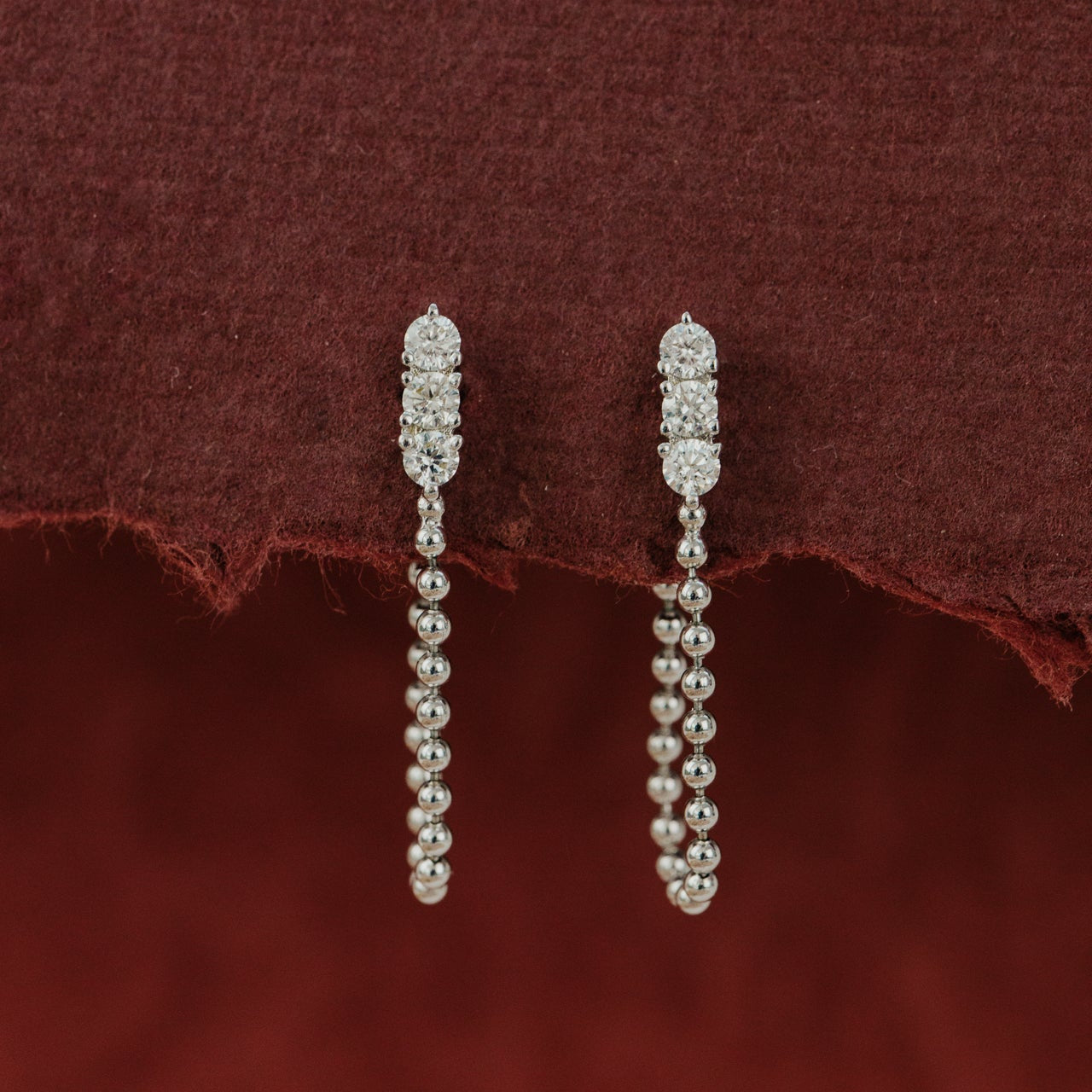 Pair of diamond drop earrings on a burgundy fabric background