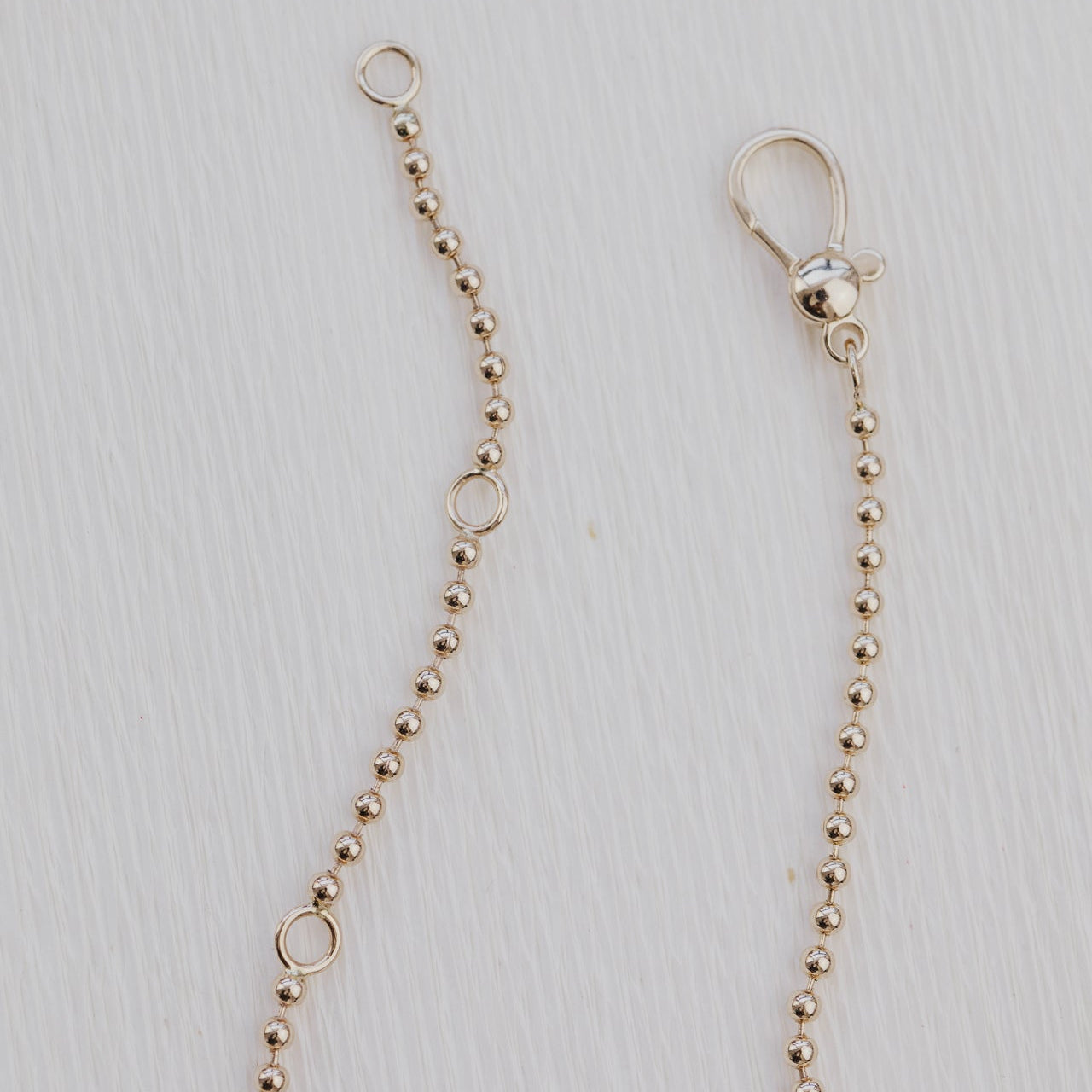 Gold beaded chain with clasp on a light gray background