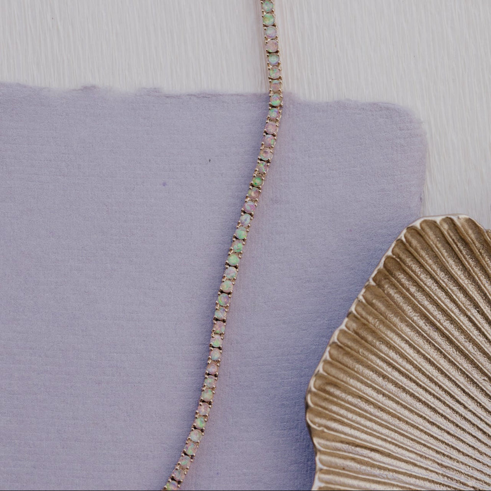 Close-up of a opal necklace with a scallop shell on a textured purple background
