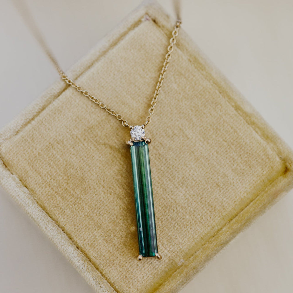 Necklace with a green tourmaline pendant and diamond on a beige cushion