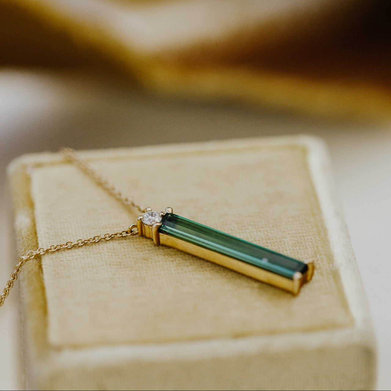 Gold necklace with a green tourmaline pendant on a beige jewelry box