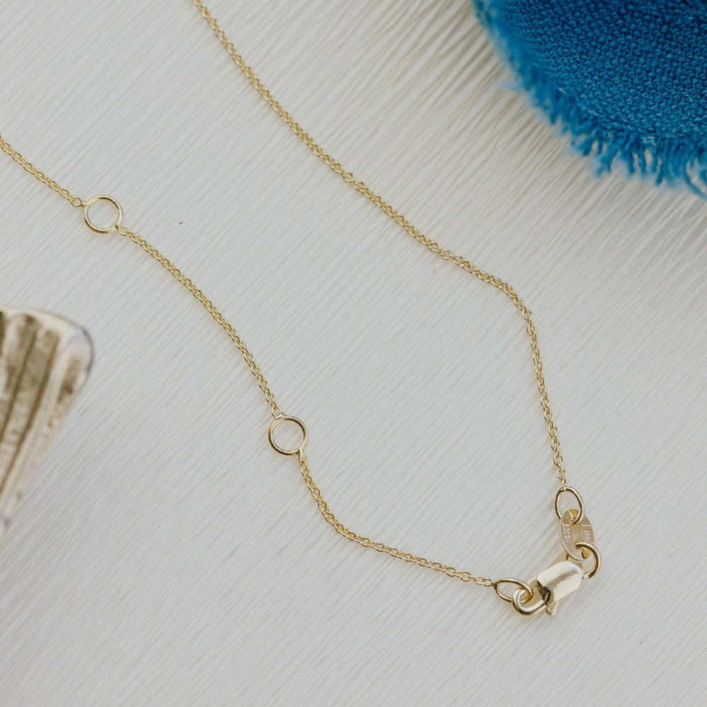 Gold necklace on a textured white surface with a blue fabric item in the corner