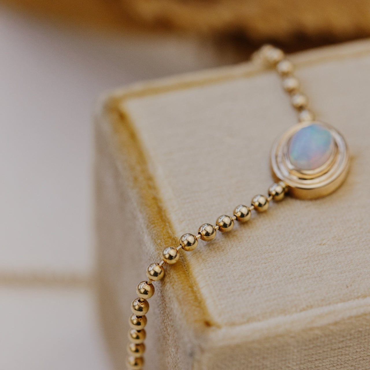 Gold necklace with an opal pendant on a beige box