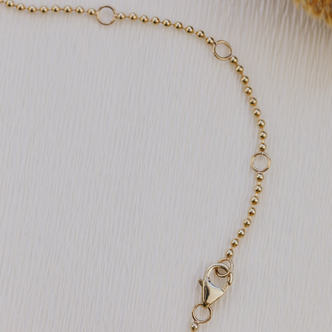 Gold beaded necklace with clasp on a light fabric background