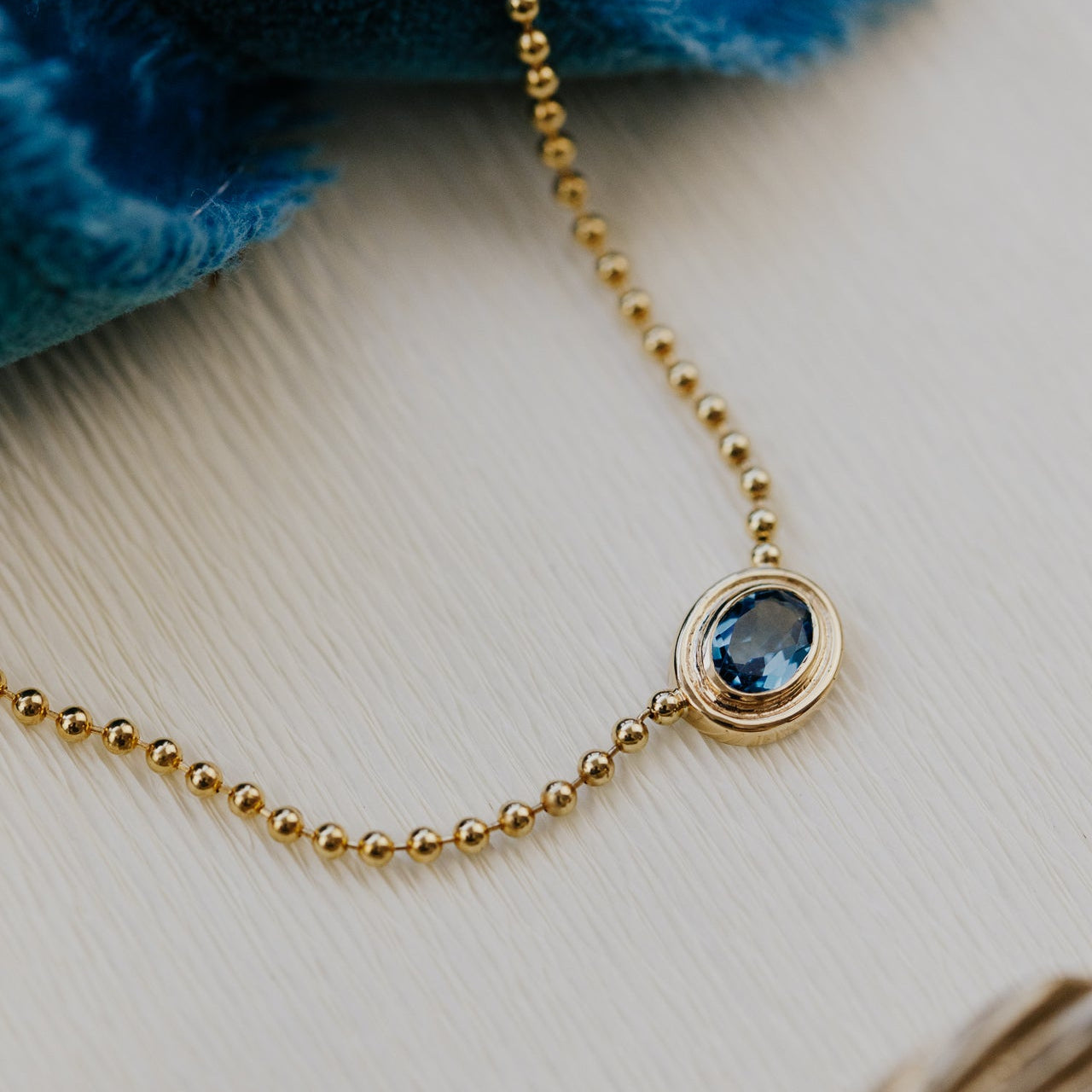Gold necklace with a blue topaz gemstone pendant on a light wooden surface
