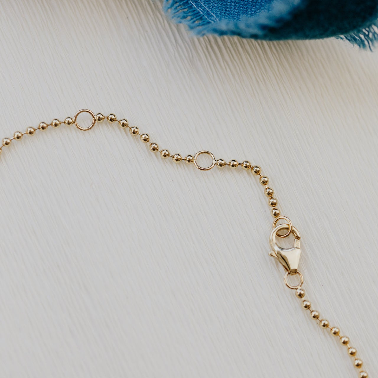 Gold beaded necklace on a textured surface with a blue fabric item in the background