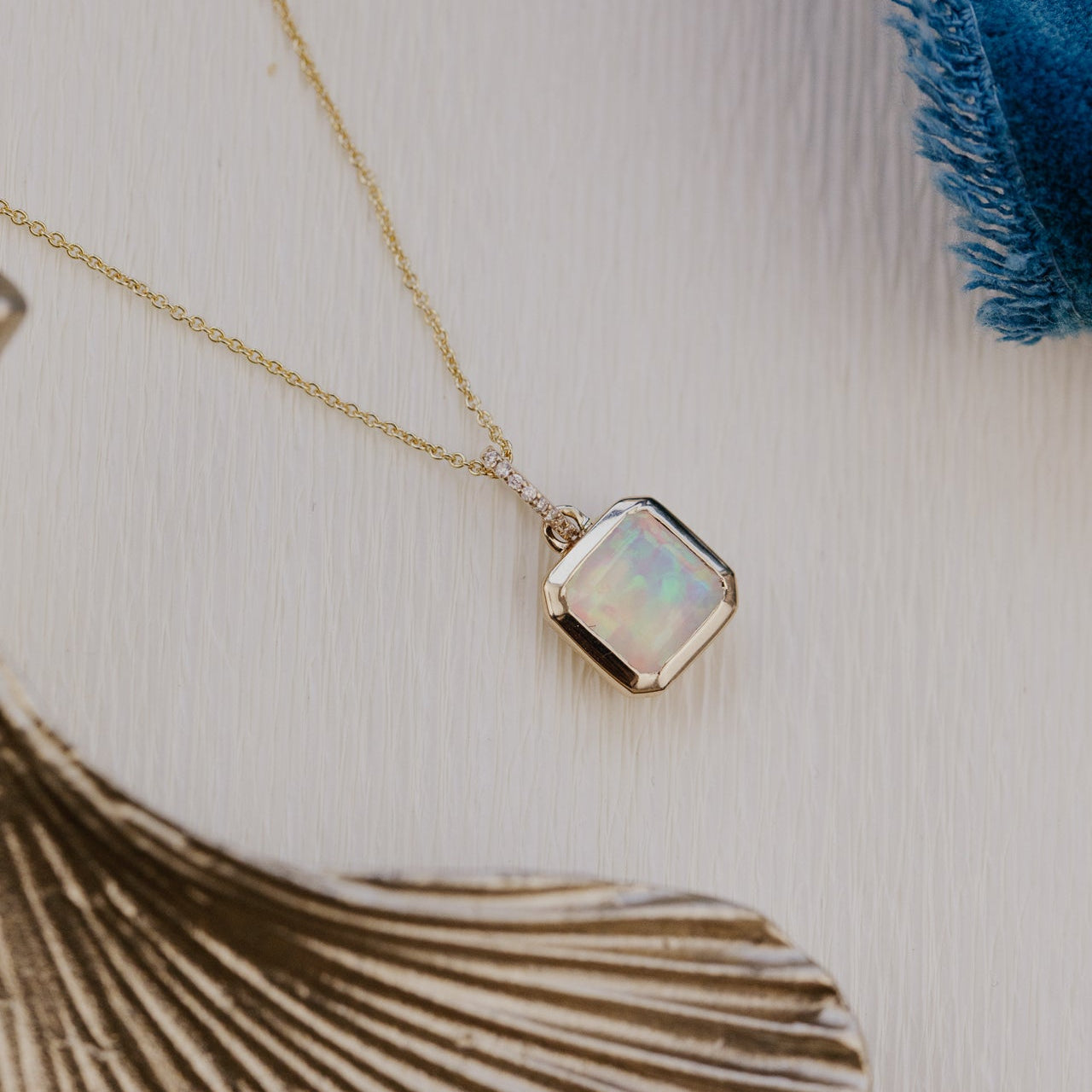 Necklace with a square opal pendant on a textured surface with a blue and brown leaf