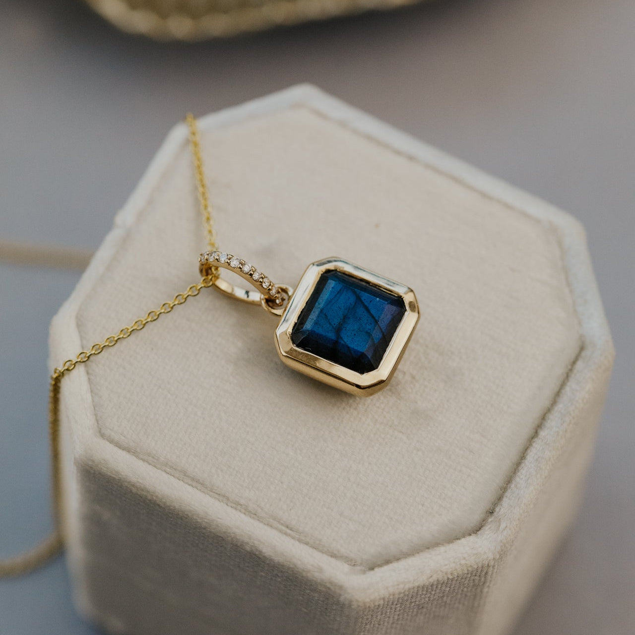 Gold necklace with a blue labradorite pendant on a beige cushion