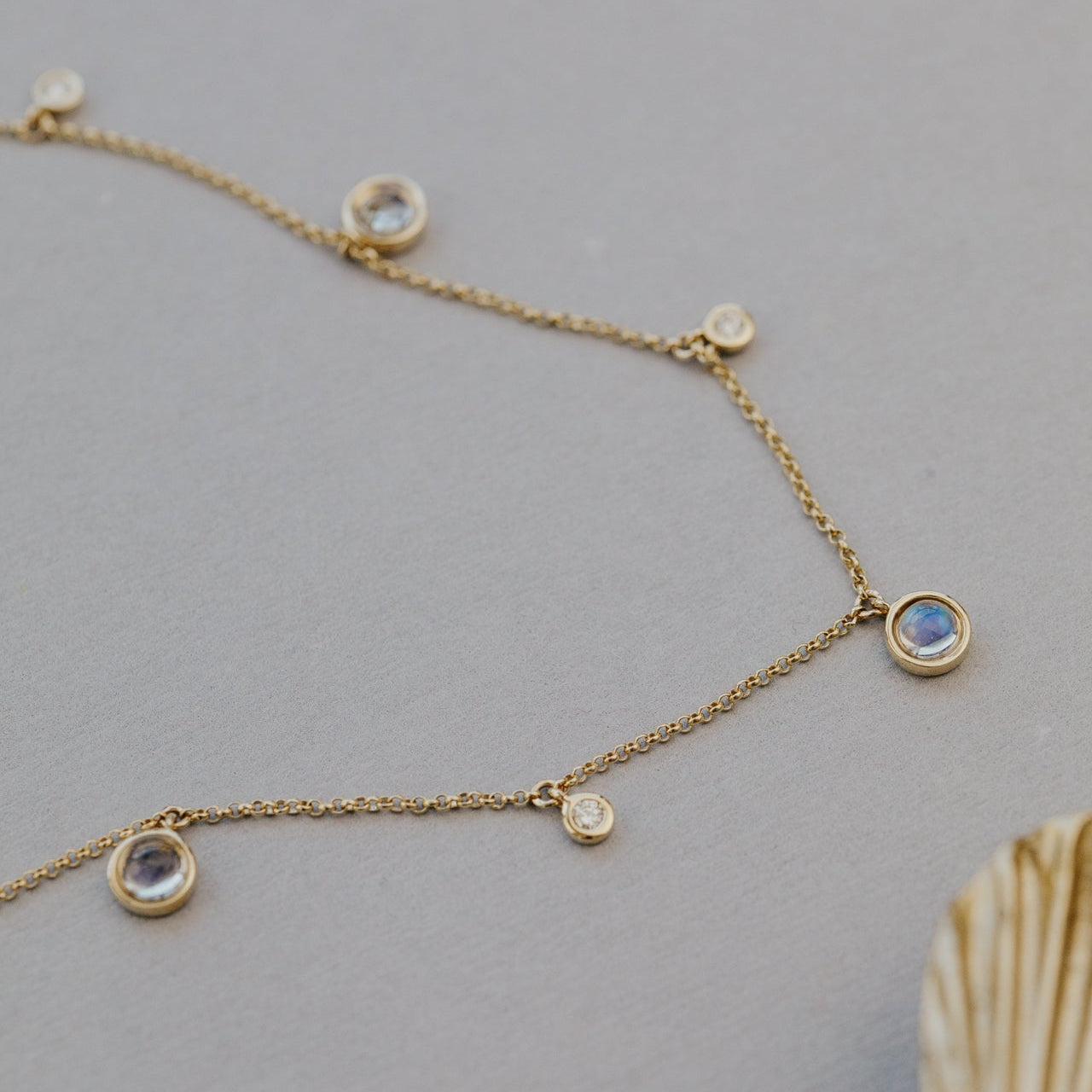Gold necklace with moonstone and diamond  pendants on a gray background