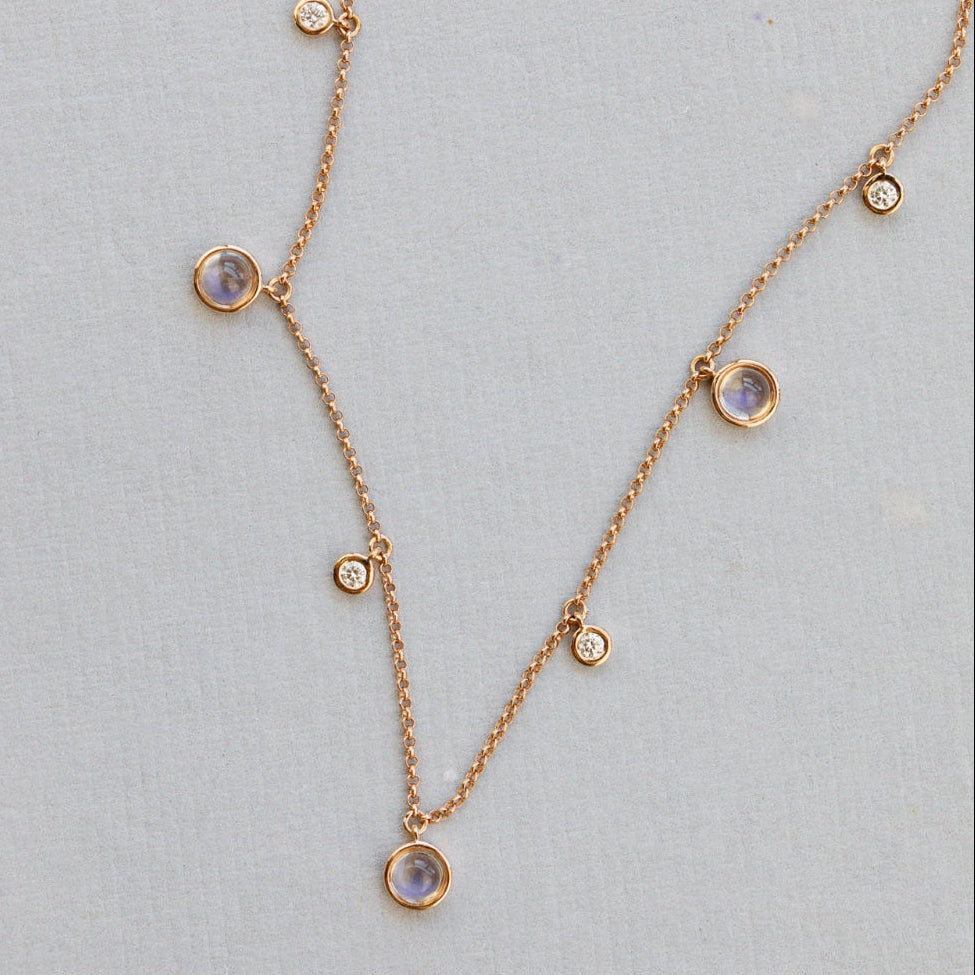 Rose gold necklace with moonstone and diamond gemstone pendants on a light gray background