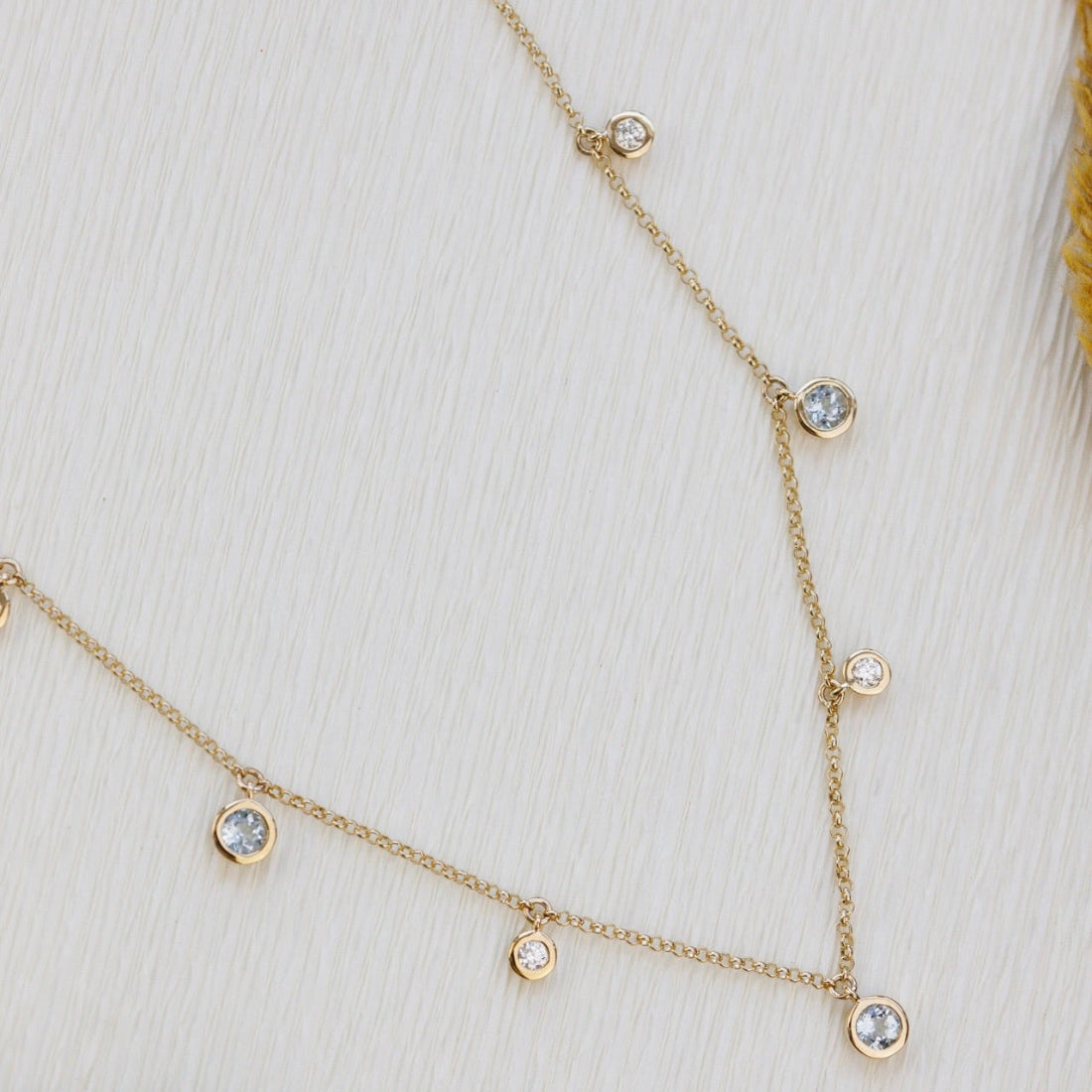Delicate gold necklace with aquamarine and diamond gemstones on a white background