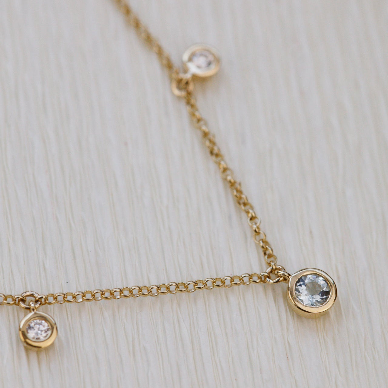 Gold necklace with round aquamarine and diamond gemstones on a light wooden surface