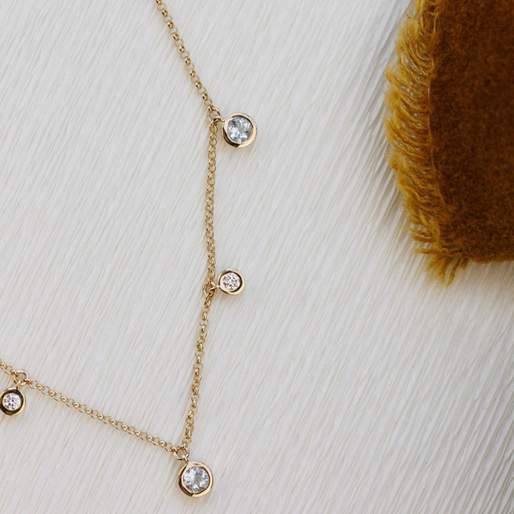 Gold necklace with aquamarine and diamonds on a textured white surface