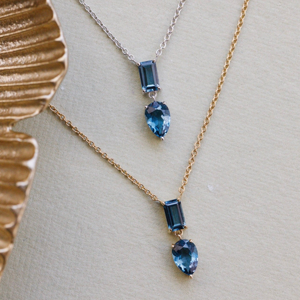 Two necklaces with blue topaz gemstones on a beige surface