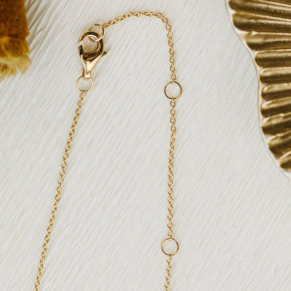 Gold chain necklace on a textured white surface with a gold decorative object in the background