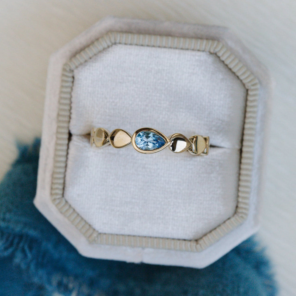 Gold ring with a blue gemstone in a jewelry box on a textured surface