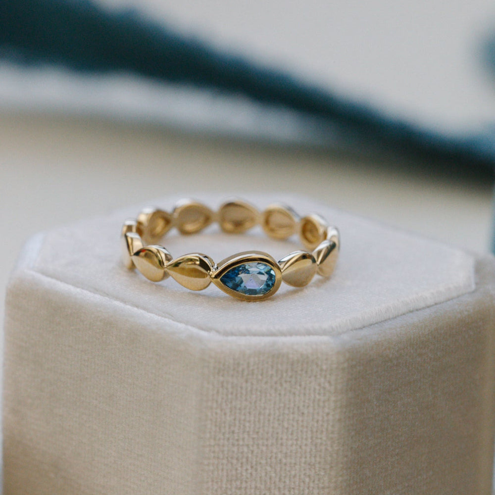 Gold ring with a blue gemstone on a beige cushion