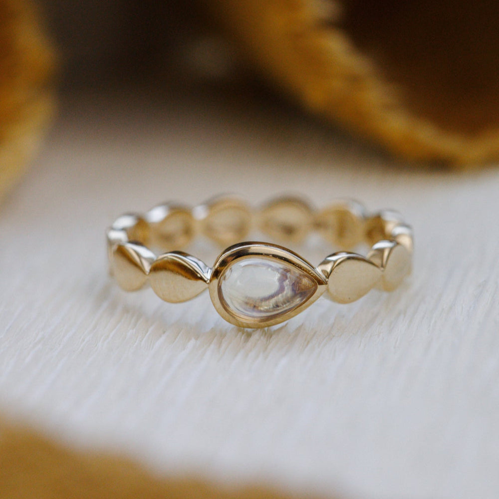Gold ring with a central pear-shaped gemstone on a light wooden surface.