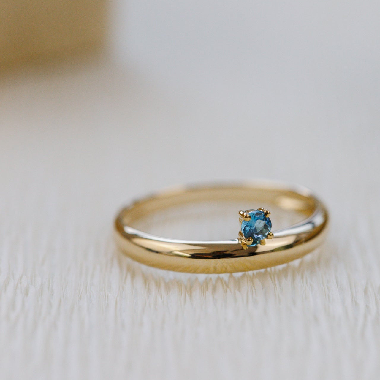 Gold ring with a blue gemstone on a light wooden surface