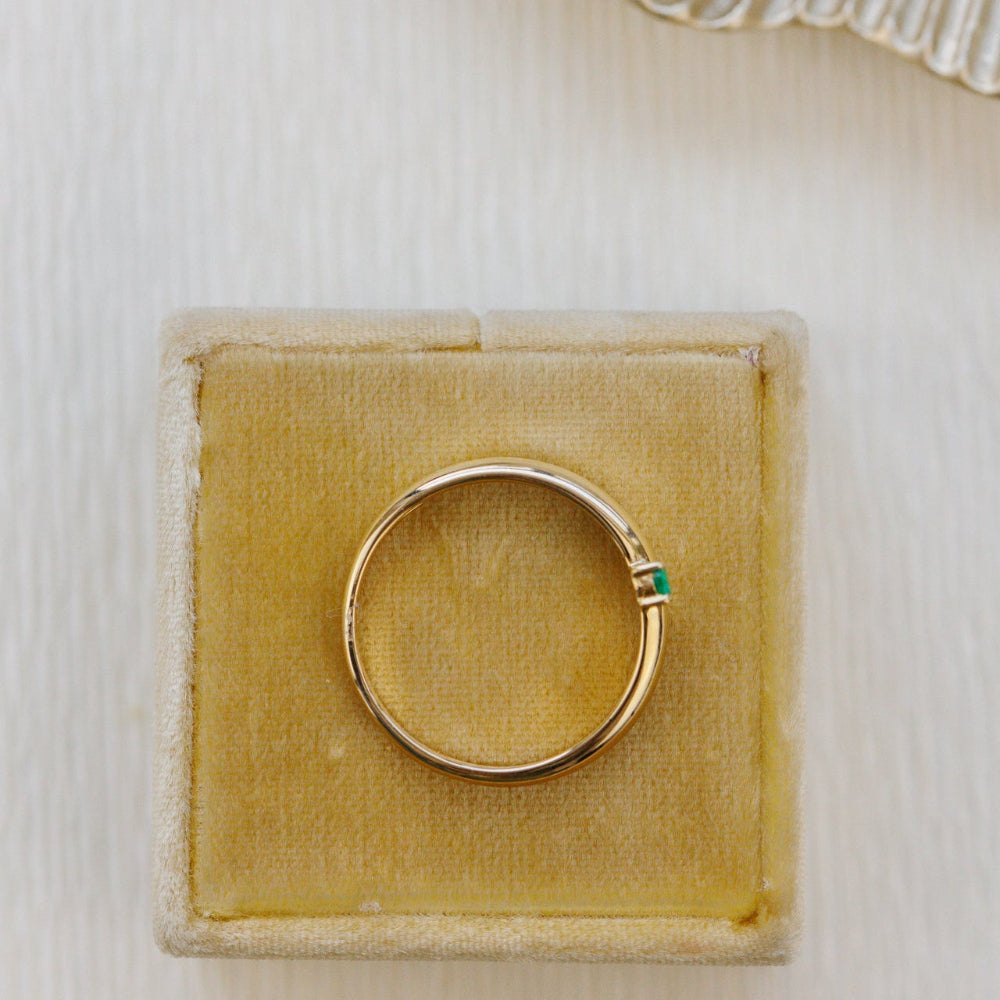 Gold ring with a green gemstone on a yellow velvet cushion