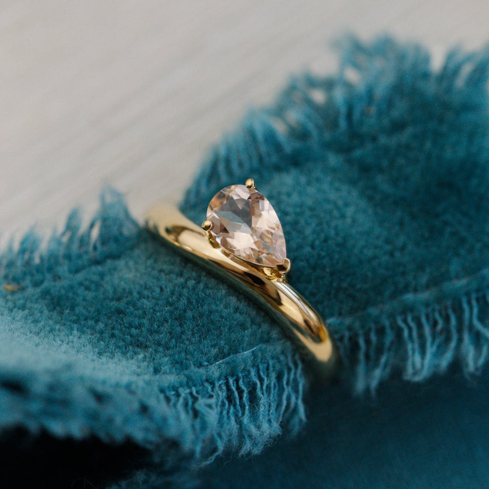 Gold ring with a pear-shaped gemstone on a blue textured surface