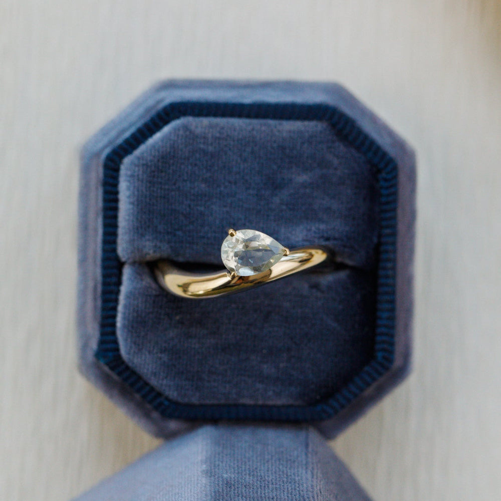 Gold ring with a green gemstone in a blue velvet box on a light wooden surface
