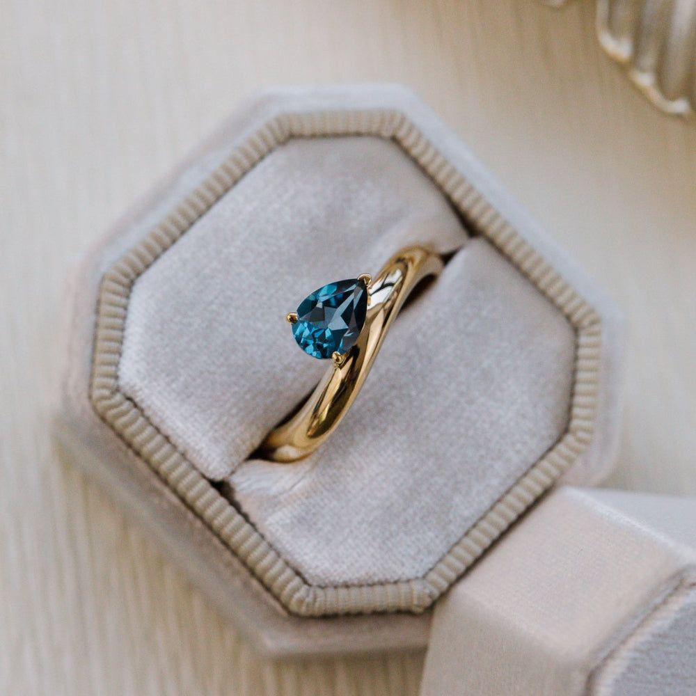 Gold ring with a blue gemstone in a hexagonal jewelry box on a beige background