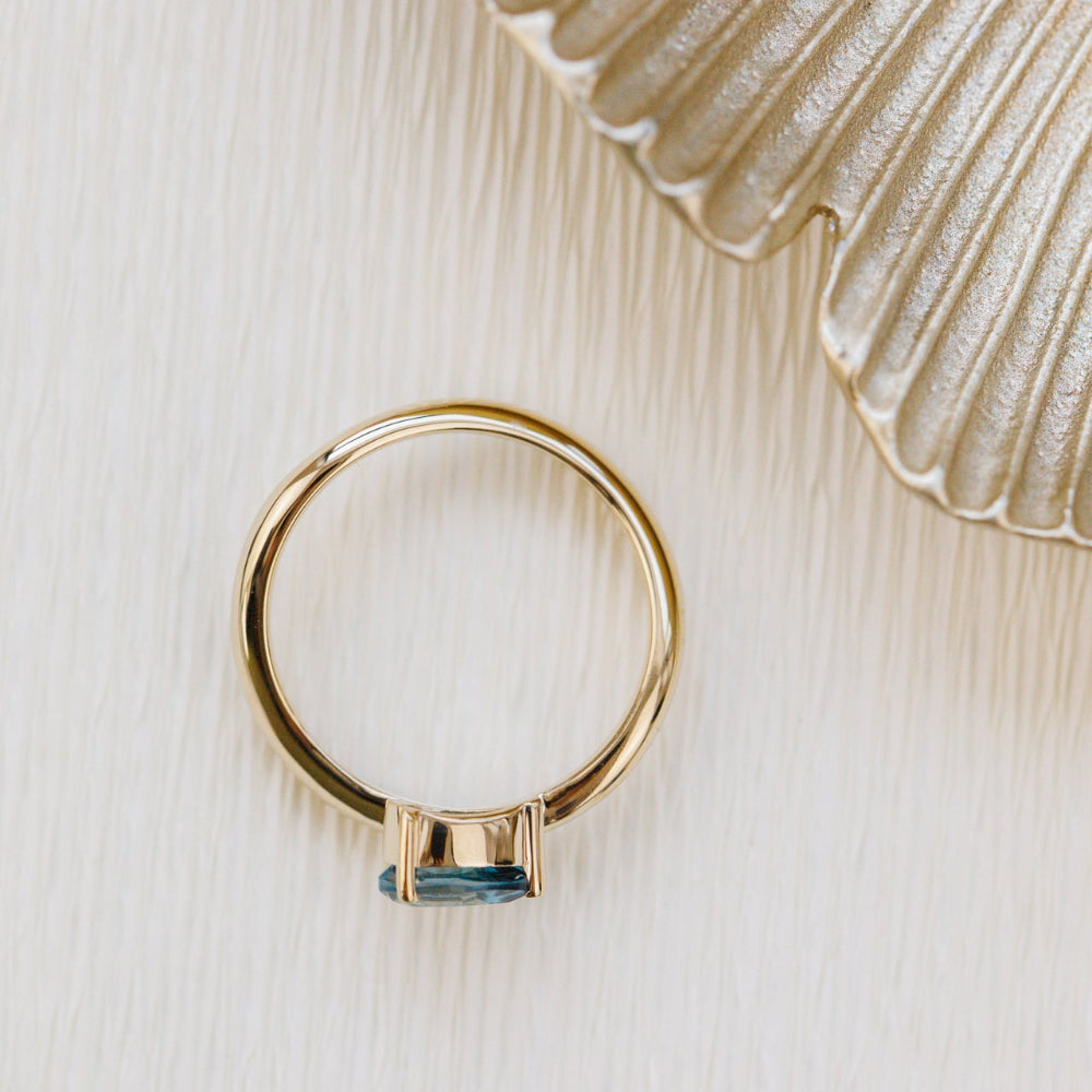 Gold ring with a blue gemstone on a textured beige surface