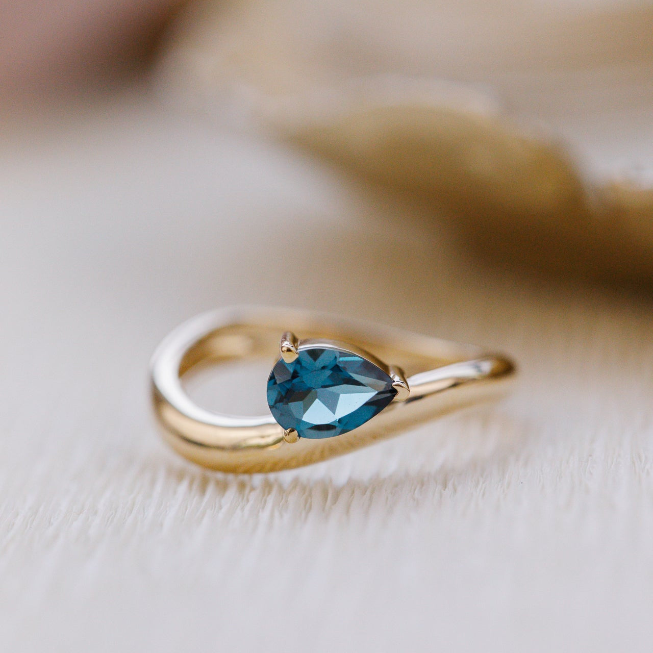 Gold ring with a blue gemstone on a soft beige background