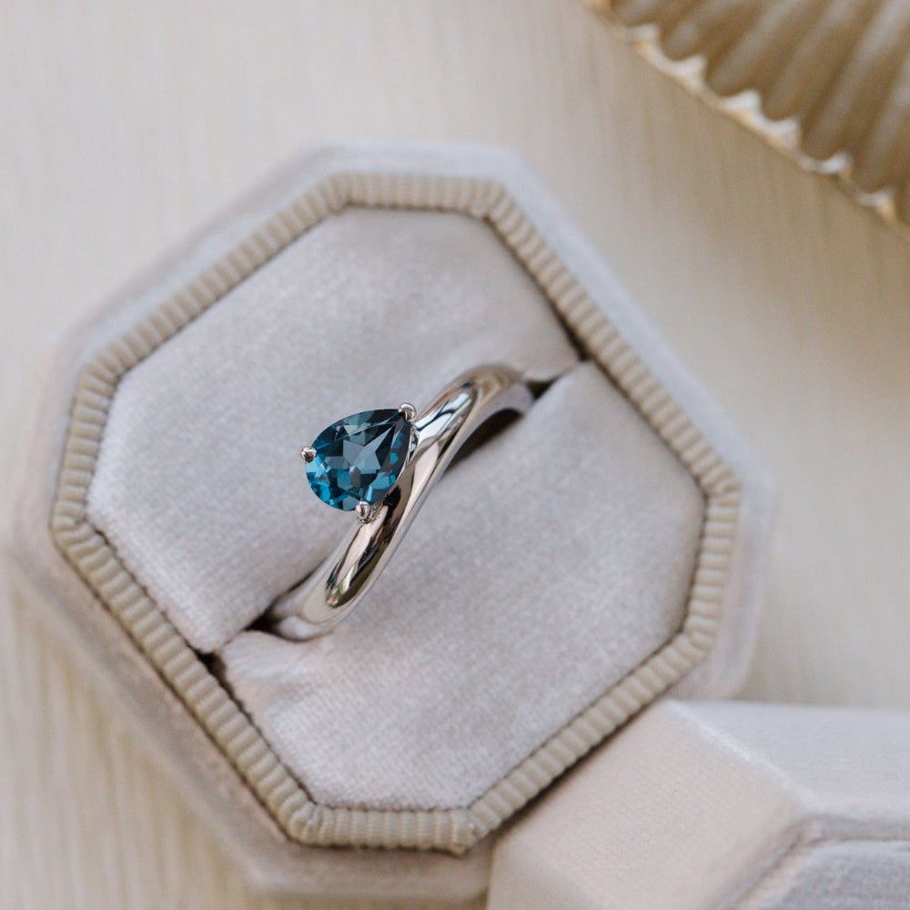 White gold ring with a blue gemstone in a hexagonal box on a beige background