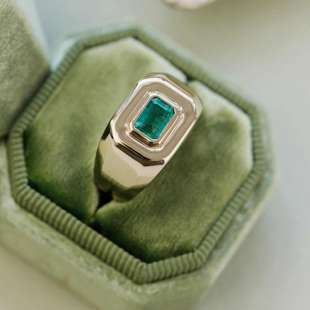 Silver ring with a green emerald gemstone on a green velvet cushion