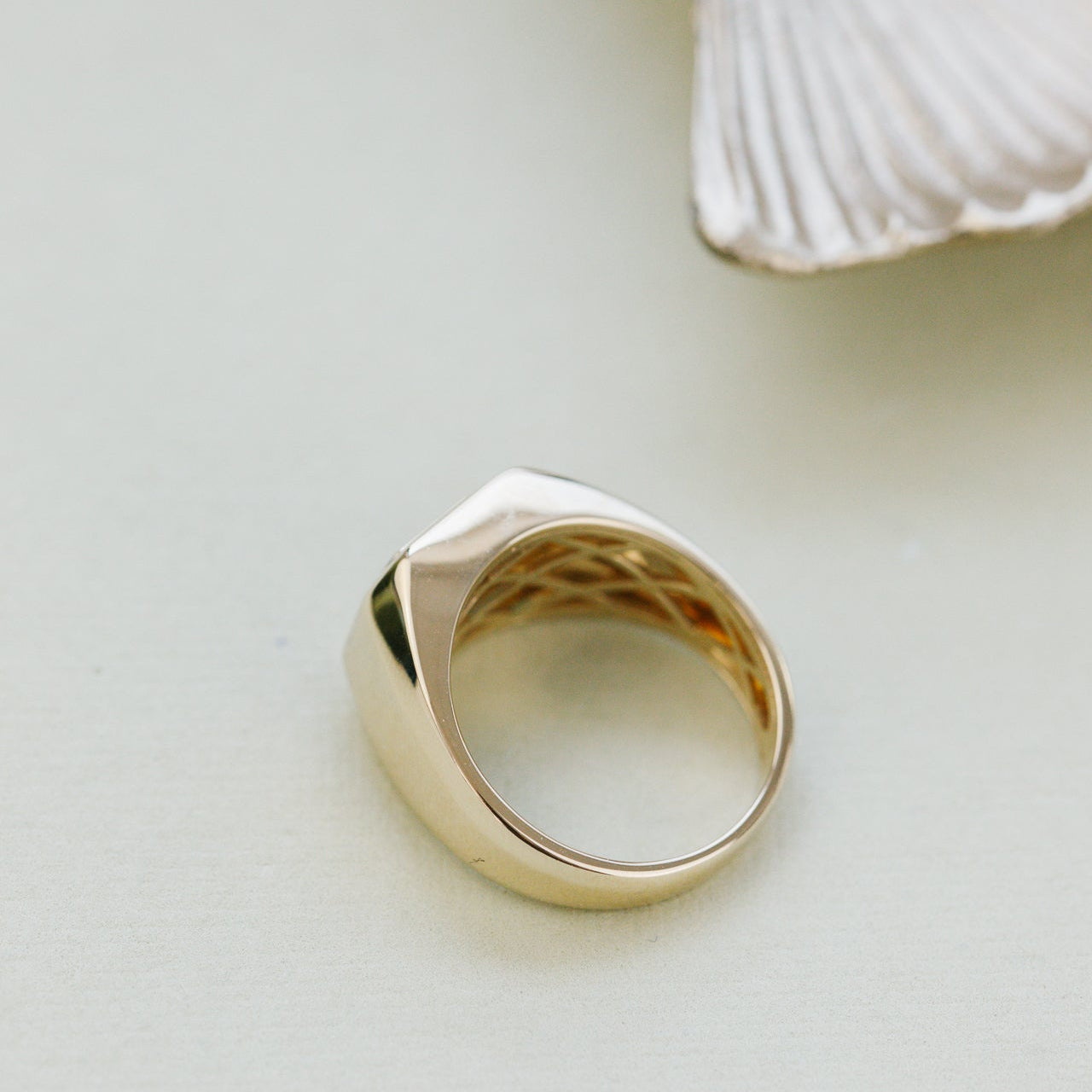 Gold ring on a light beige surface with a shell in the background