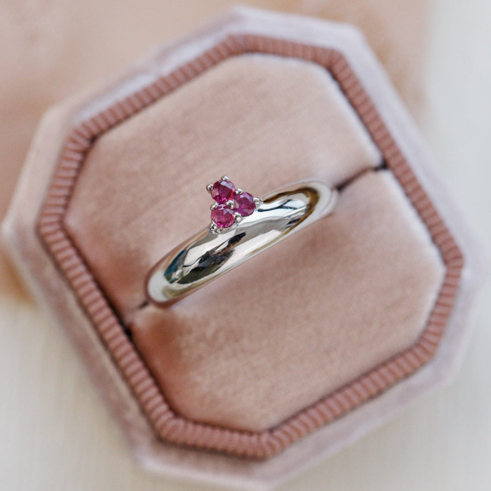 White gold ring with ruby gemstones on a pink velvet cushion
