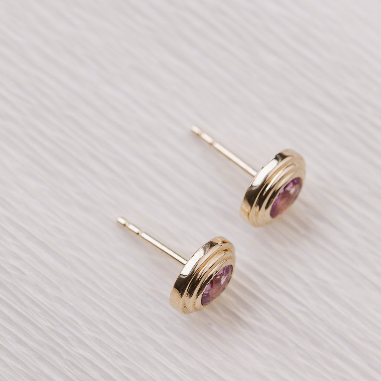 Gold earrings with pink gemstones on a light gray background