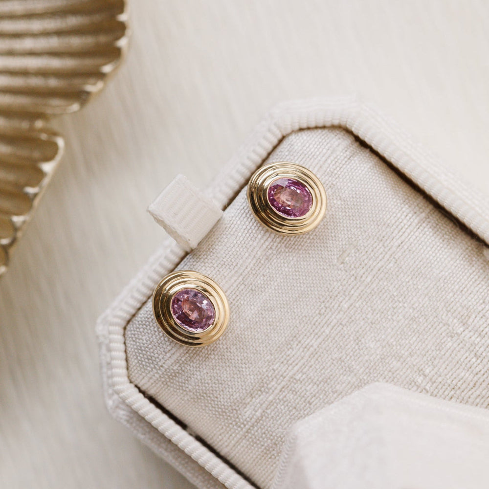Close-up of a beige jacket with gold earrings featuring pink gemstones.
