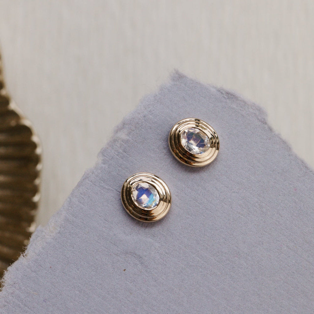 Gold earrings with gemstones on a gray surface