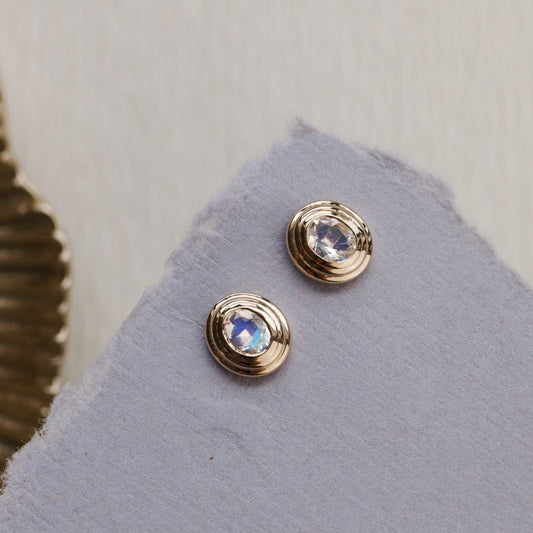 Gold earrings with gemstones on a gray surface
