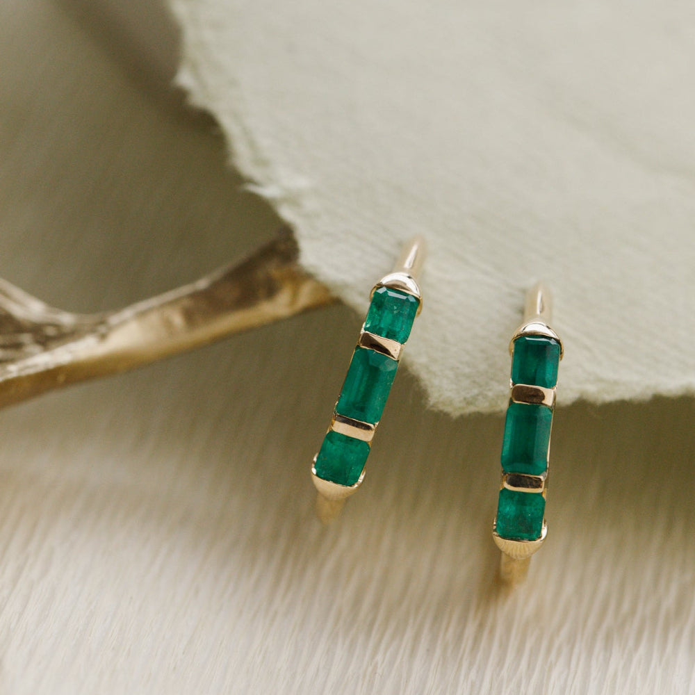 Green emerald earrings with gold accents on a textured beige surface