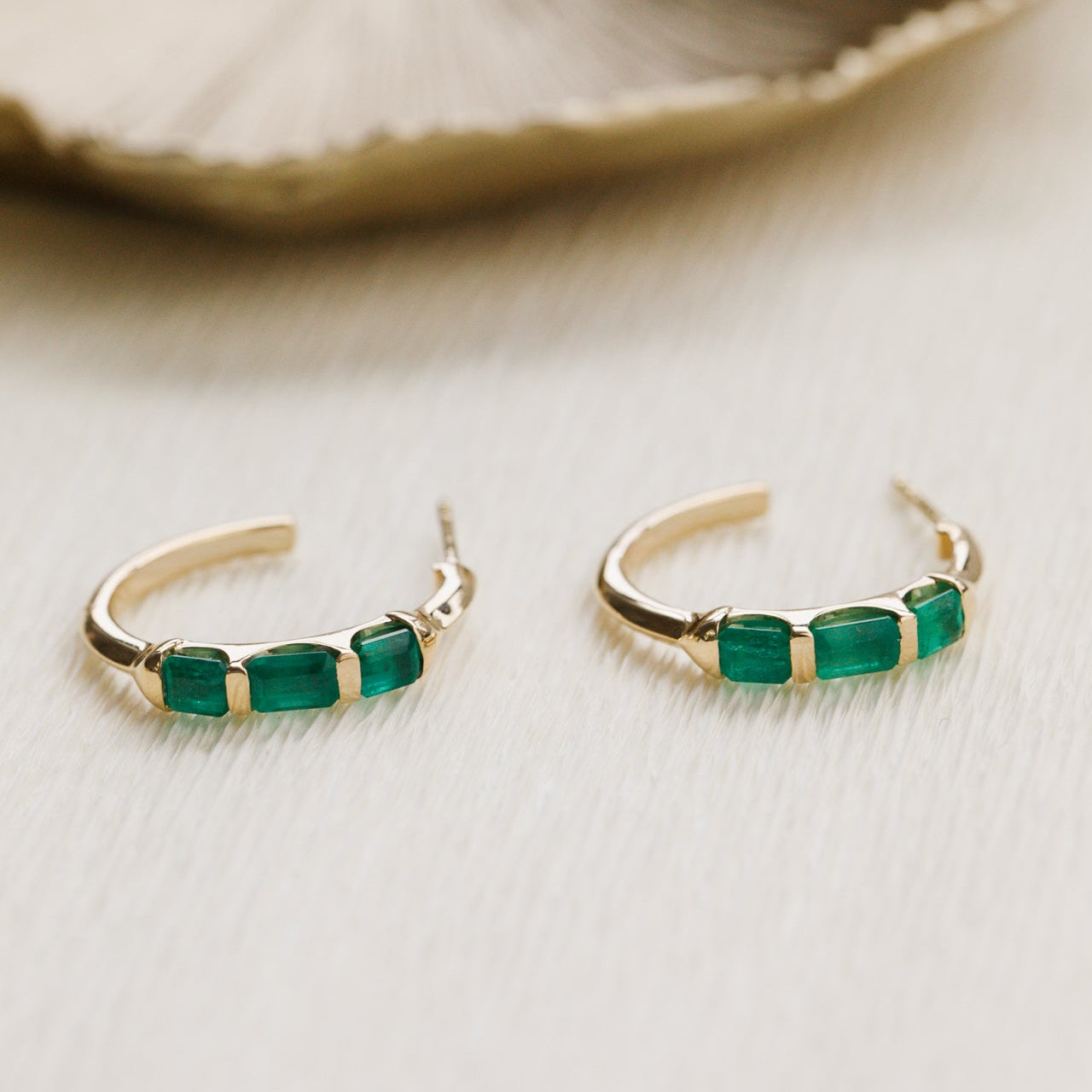 Gold hoop earrings with green gemstones on a neutral background